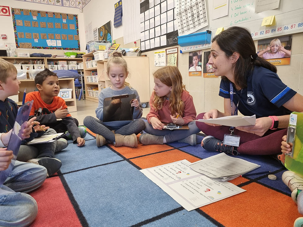 children sitting in a circle on a rug and reading with their teacher